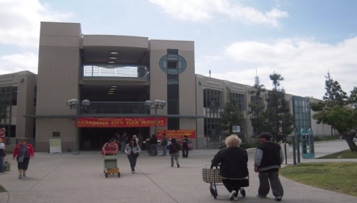 Exterior view of the Pasadena City Flea Market, with people walking and shopping in front of the building.