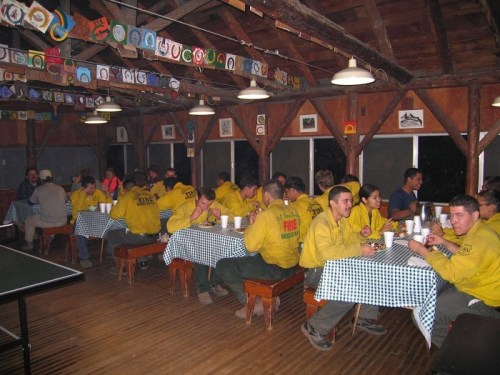A group of people in yellow shirts sitting at tables in a rustic dining hall, enjoying a meal together.