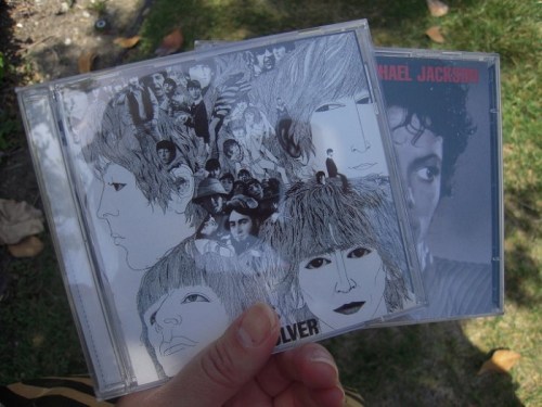 A hand holding two CD cases: one featuring a collage of faces and the other with a close-up of a singer.