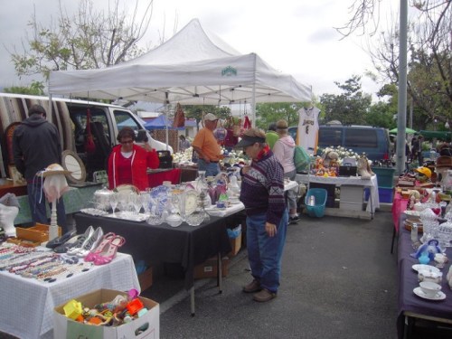 A bustling outdoor market with vendors selling various items under a tent, including antiques and crafts.