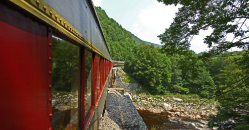 A scenic view from a train window, showcasing lush green mountains and a river below.