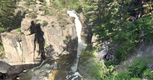 A waterfall cascading between rocky cliffs, surrounded by lush green trees and sunlight filtering through the foliage.