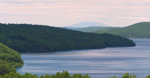 A serene landscape featuring a calm lake surrounded by lush green hills under a cloudy sky.