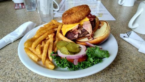 A hearty burger topped with cheese, bacon, and a crispy onion ring, served with fries and a side salad.