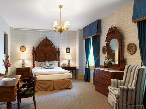 A cozy bedroom featuring a wooden bed, vintage furniture, blue curtains, and decorative mirrors.