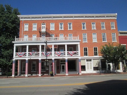 Historic brick building with a white balcony, decorated with red, white, and blue bunting, under a clear blue sky.