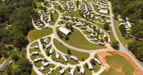 Aerial view of a campground with winding roads, RVs, and green spaces surrounded by trees.