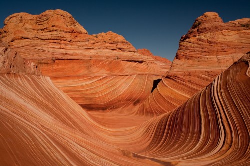 Vibrant sandstone formations with wavy, colorful stripes under a clear blue sky in a desert landscape.