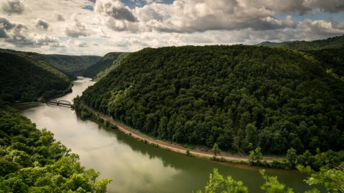 A scenic view of a winding river surrounded by lush green hills under a cloudy sky.
