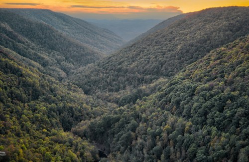 A scenic view of a lush green valley surrounded by mountains at sunset, with a river winding through the landscape.
