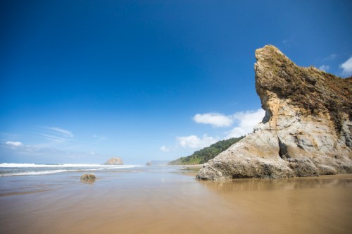 A sandy beach with rocky cliffs under a clear blue sky and gentle waves lapping at the shore.