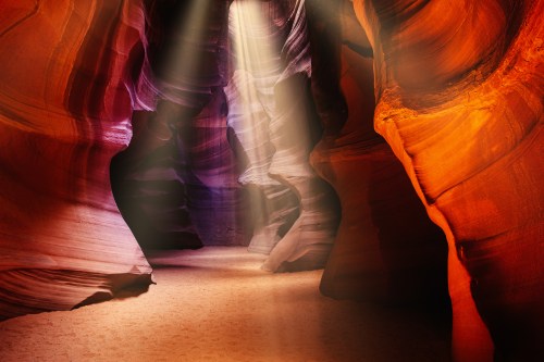 A stunning view of Antelope Canyon with vibrant red and purple rock formations illuminated by beams of sunlight.