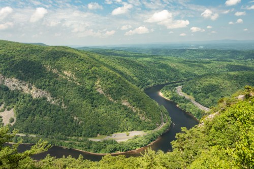 A scenic view of a winding river surrounded by lush green hills under a partly cloudy sky.