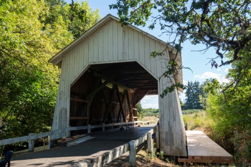 A wooden covered bridge surrounded by trees, with a clear blue sky in the background.