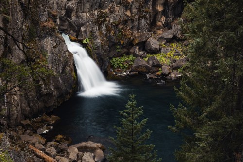 A serene waterfall cascades into a tranquil pool, surrounded by rocky cliffs and lush greenery.