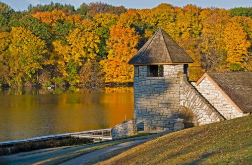 Stone tower by a lake surrounded by vibrant autumn foliage in shades of orange and yellow.