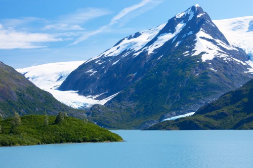 A serene landscape featuring a turquoise lake, lush greenery, and snow-capped mountains under a clear blue sky.