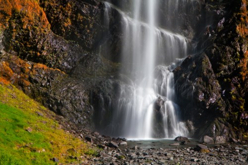 A serene waterfall cascading over rocky cliffs, surrounded by lush greenery and vibrant autumn foliage.