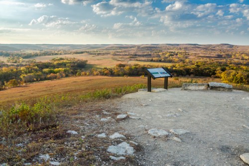 Scenic view of rolling hills and fields under a cloudy sky, with an informational sign in the foreground.