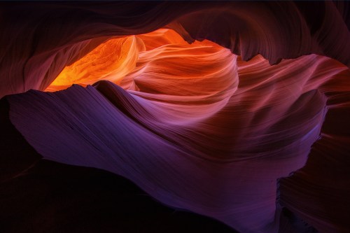 A stunning view of colorful, swirling rock formations illuminated by warm light in a narrow canyon.