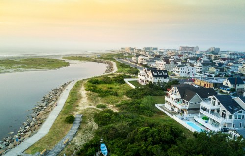 Aerial view of a coastal town at sunset, featuring houses, a river, and a sandy path along the shore.