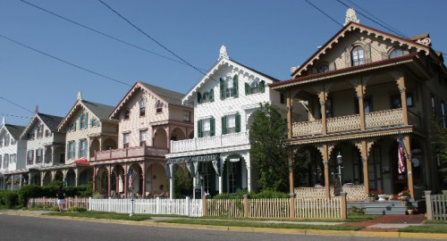 A row of colorful Victorian-style houses with intricate details and porches, set against a clear blue sky.