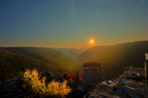 Sunset over a valley, with colorful foliage and rocky outcrops in the foreground, creating a serene landscape.