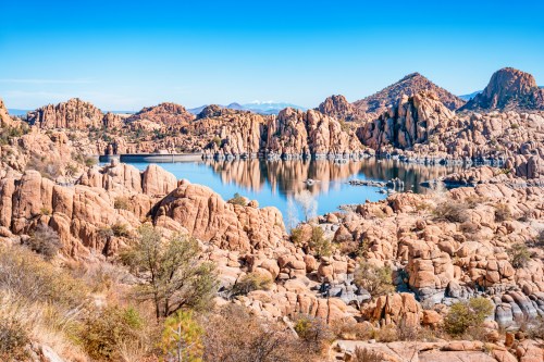 Scenic view of rocky formations and a calm lake, surrounded by mountains under a clear blue sky.