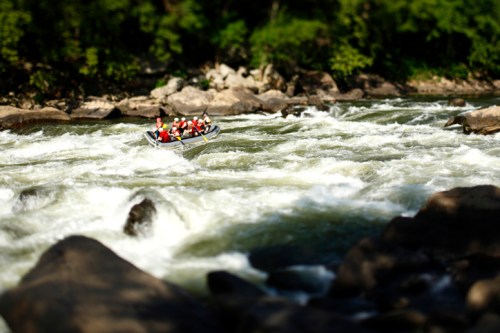 A group of people in a raft navigating through turbulent whitewater rapids surrounded by rocky terrain and greenery.