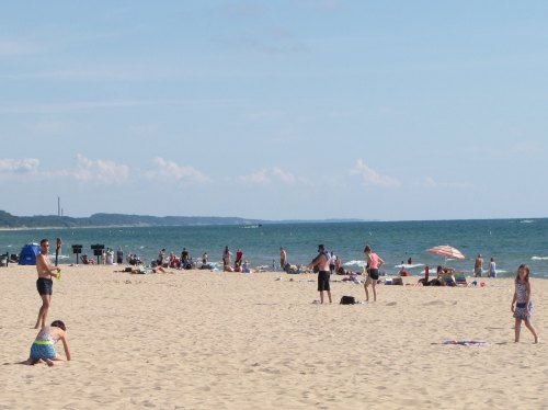 A sunny beach scene with people sunbathing, playing, and relaxing on the sand near the water.