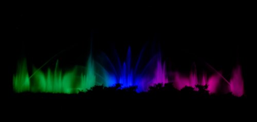 Colorful water fountains illuminated in green, blue, and pink against a dark background.