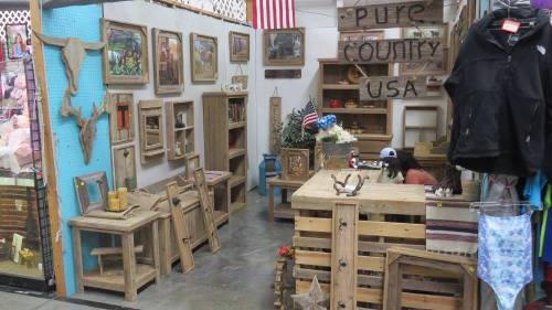 A rustic shop interior featuring wooden furniture, decor, and a person working at a table, with American flags displayed.