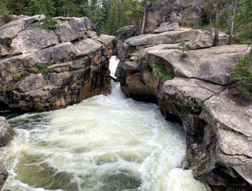A rushing river flows between rocky cliffs, surrounded by lush greenery and trees.