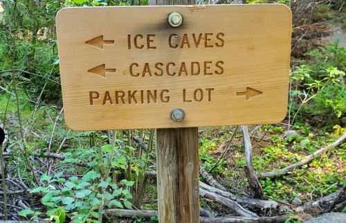 Wooden signpost with arrows pointing to Ice Caves, Cascades, and Parking Lot in a forested area.