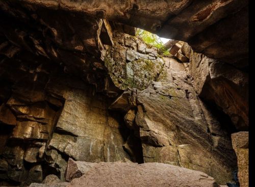 A rocky cave with towering stone walls and a small opening at the top, allowing light to filter in.