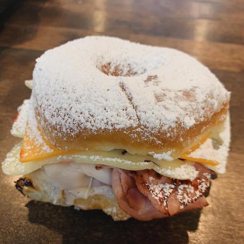 A sandwich made with a powdered sugar-coated donut, layered with cheese, ham, and turkey.