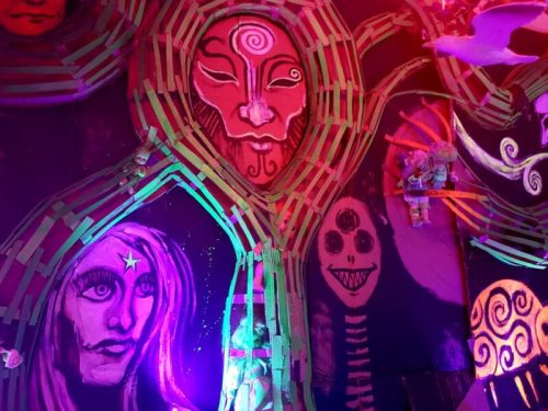 Colorful mural featuring stylized faces and figures, illuminated with vibrant lights and intricate designs.