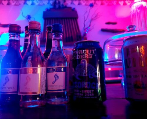 A colorful display of various wine bottles and a cider can on a table, illuminated by vibrant lights.