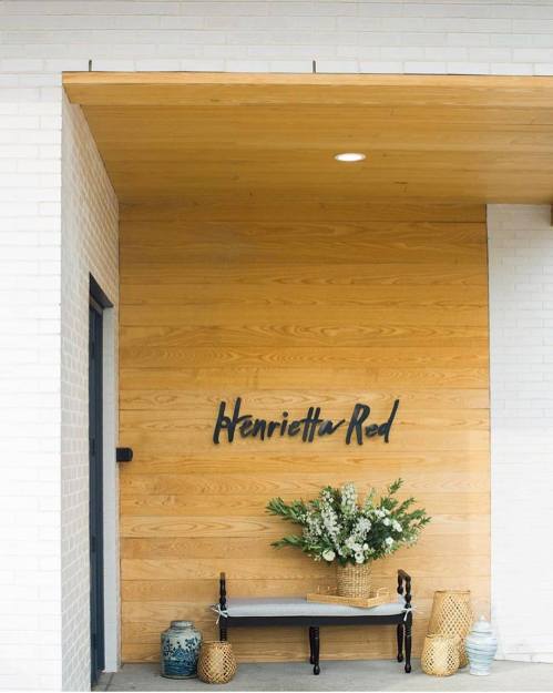 A welcoming entrance with a wooden wall, "Henrietta Red" sign, floral arrangement, and decorative baskets.