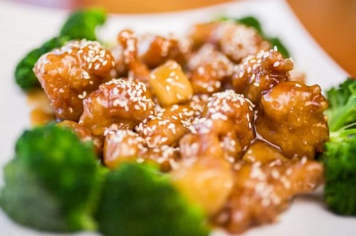 A plate of sesame chicken with broccoli, featuring tender pieces in a glossy sauce and sprinkled with sesame seeds.