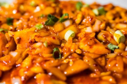 Close-up of a vibrant dish featuring diced chicken in a spicy orange sauce, garnished with green onions.