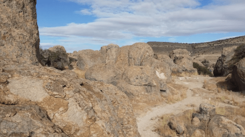 Rocky landscape with large boulders and sparse vegetation under a blue sky with scattered clouds.