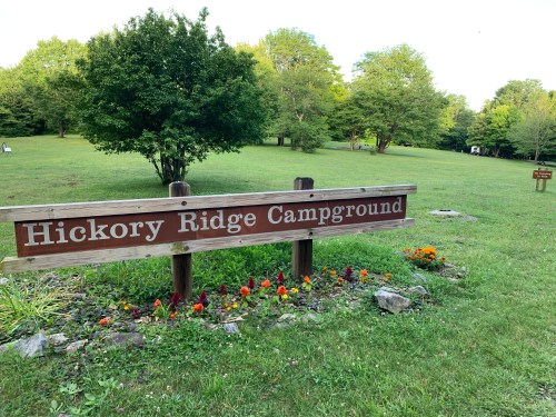 Sign for Hickory Ridge Campground in a grassy area with trees and colorful flowers in the foreground.