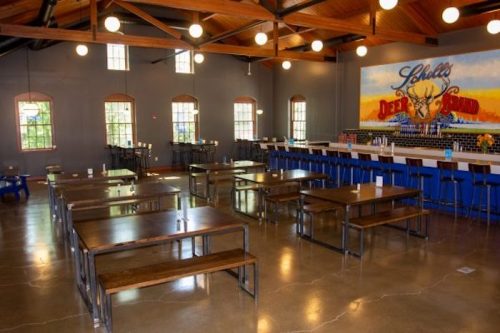 A spacious dining area with wooden tables, benches, and a colorful mural on the wall, featuring a bar in the background.