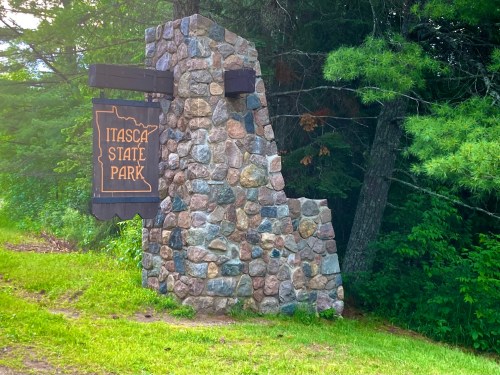 Stone sign for Itasca State Park surrounded by trees and greenery.