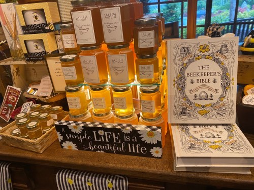 A display of honey jars and "The Beekeeper's Bible" book on a wooden table, with decorative signs.
