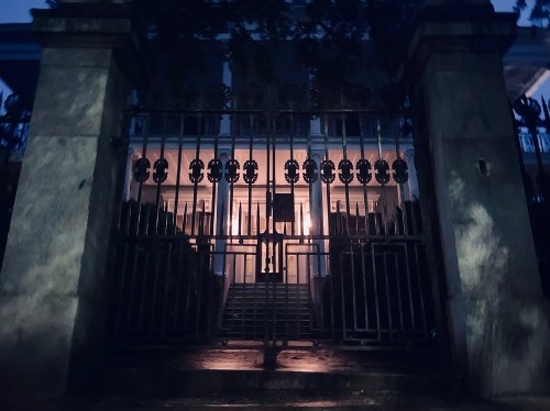 A dimly lit entrance gate to a large, shadowy building at night, surrounded by trees.