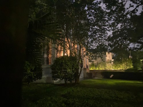 A dimly lit building surrounded by trees at night, with soft light illuminating part of the facade.