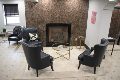 Cozy seating area with two black chairs, a gold coffee table, and a fireplace against a textured wall.
