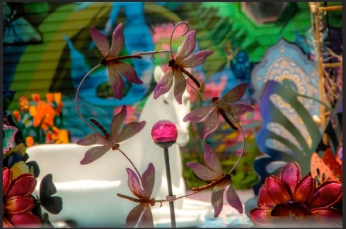 Colorful garden scene featuring decorative flowers and dragonflies, with a whimsical background of vibrant patterns.
